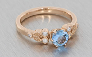 Rose gold ring set with an Aquamarine with small white diamonds and milgrain detailing