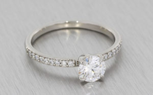 Round brilliant diamond ring housed in a 4 claw setting with grain set diamond shoulders